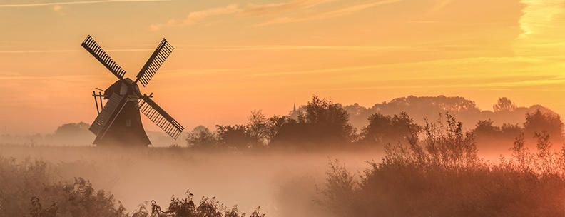 Nebliger Sonnenaufgang in einem Feuchtgebiet in der Nähe einer traditionellen Windmühle in Holland